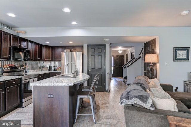 kitchen with a breakfast bar, sink, dark brown cabinets, a center island with sink, and stainless steel appliances