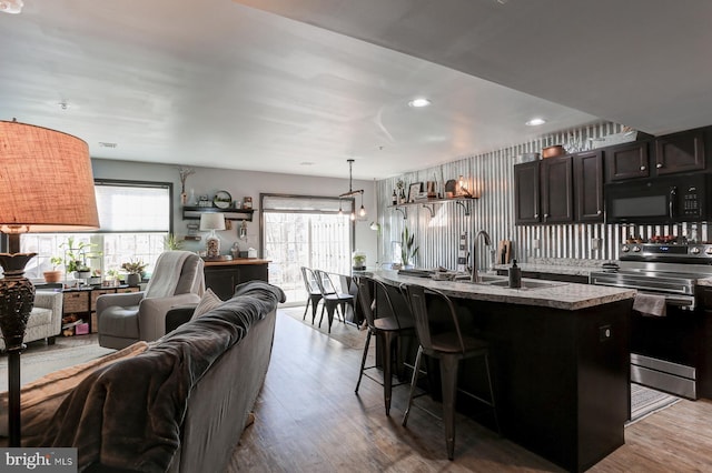 kitchen featuring sink, stainless steel range with electric stovetop, dark brown cabinets, a kitchen breakfast bar, and a center island with sink