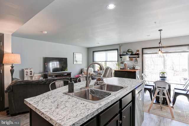 kitchen with sink, light hardwood / wood-style flooring, dishwasher, an island with sink, and pendant lighting