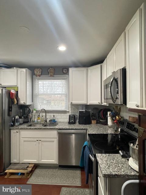 kitchen with sink, white cabinetry, light stone counters, appliances with stainless steel finishes, and backsplash