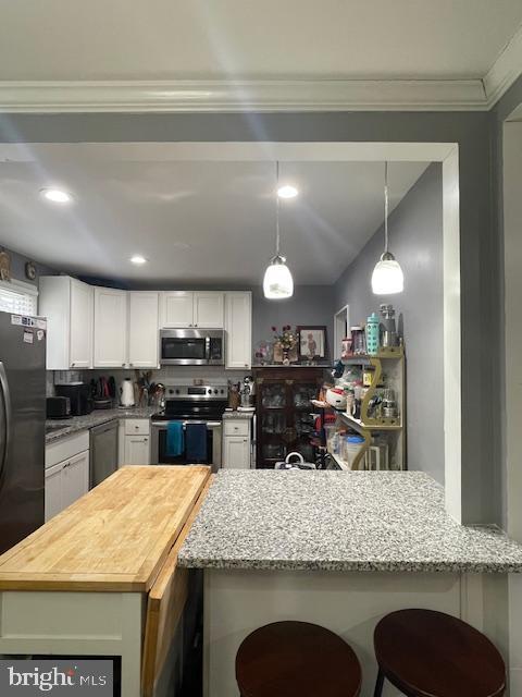 kitchen with a breakfast bar, appliances with stainless steel finishes, light stone counters, white cabinets, and kitchen peninsula