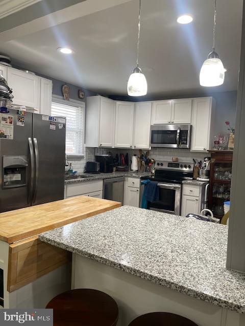 kitchen featuring hanging light fixtures, a breakfast bar area, white cabinets, and appliances with stainless steel finishes