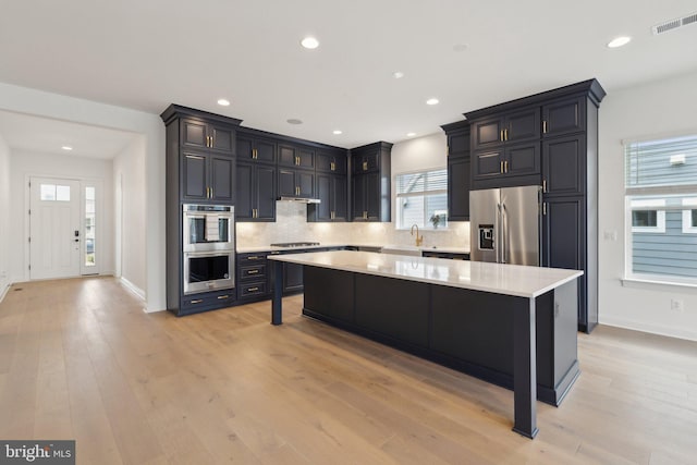 kitchen featuring light hardwood / wood-style flooring, a breakfast bar, appliances with stainless steel finishes, backsplash, and a center island