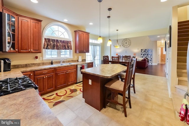 kitchen featuring appliances with stainless steel finishes, a breakfast bar, decorative light fixtures, sink, and a center island