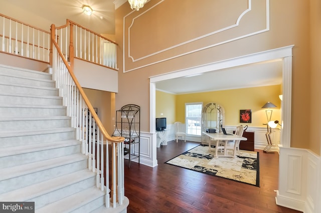 entrance foyer featuring crown molding, a towering ceiling, dark hardwood / wood-style flooring, and a notable chandelier