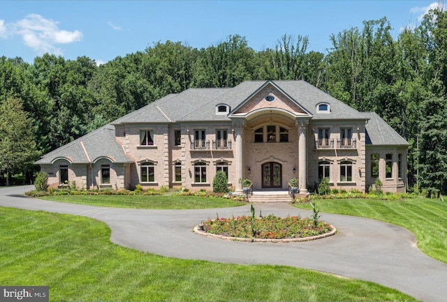 view of front of property featuring french doors, a front lawn, a balcony, and aphalt driveway