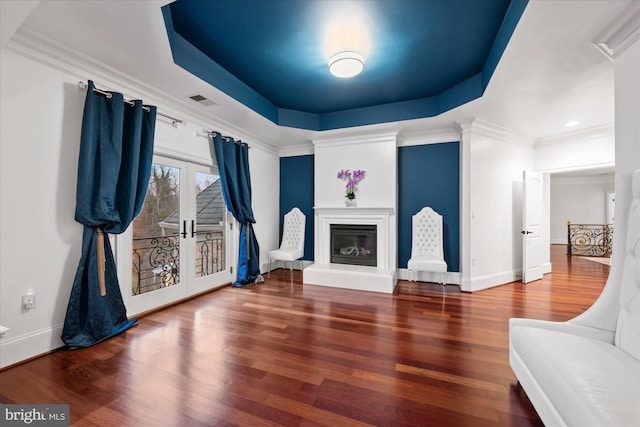 living room featuring a tray ceiling, french doors, a glass covered fireplace, and wood finished floors