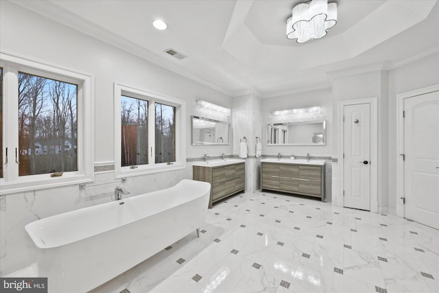 full bathroom featuring ornamental molding, a tray ceiling, a soaking tub, and two vanities