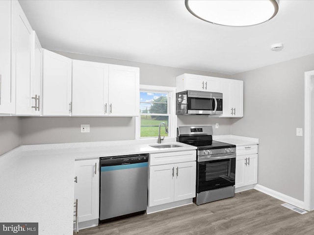 kitchen featuring appliances with stainless steel finishes, sink, white cabinets, and light hardwood / wood-style floors