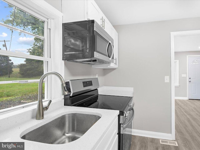 kitchen featuring sink, appliances with stainless steel finishes, white cabinetry, light stone counters, and light hardwood / wood-style floors