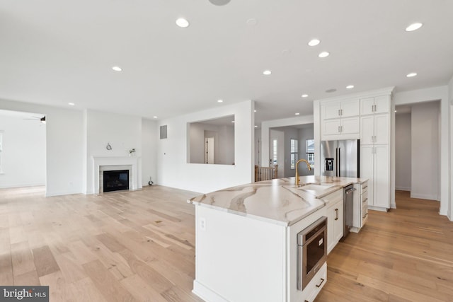 kitchen with sink, white cabinets, light stone counters, stainless steel appliances, and a center island with sink