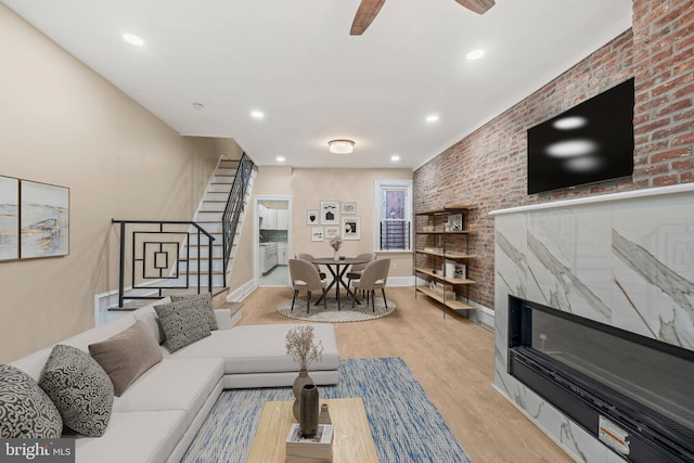 living room featuring ceiling fan, brick wall, a fireplace, and light wood-type flooring