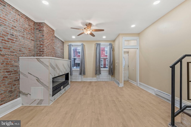 unfurnished living room with ceiling fan, brick wall, and light hardwood / wood-style flooring