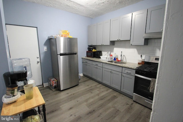 kitchen with sink, gray cabinetry, light stone counters, appliances with stainless steel finishes, and decorative backsplash