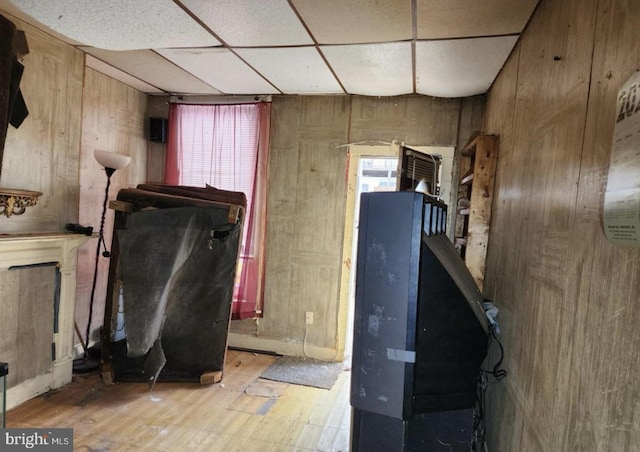 misc room featuring a drop ceiling, light hardwood / wood-style flooring, and wood walls