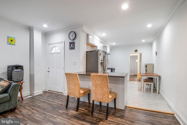 kitchen with hardwood / wood-style floors, white cabinetry, a kitchen bar, kitchen peninsula, and stainless steel refrigerator with ice dispenser