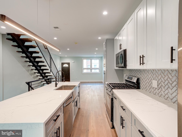 kitchen with sink, appliances with stainless steel finishes, white cabinetry, light stone counters, and decorative backsplash