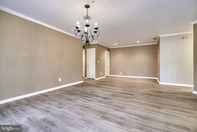 empty room with crown molding, an inviting chandelier, and light hardwood / wood-style floors