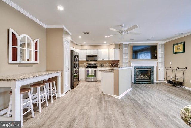 kitchen with a kitchen bar, light stone counters, appliances with stainless steel finishes, kitchen peninsula, and white cabinets