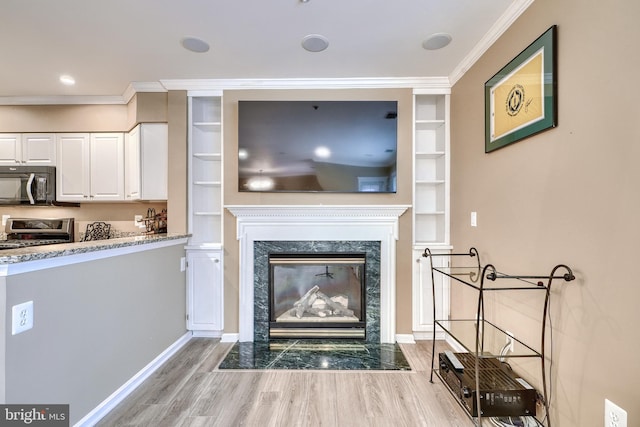 living room featuring crown molding, a high end fireplace, built in features, and light wood-type flooring