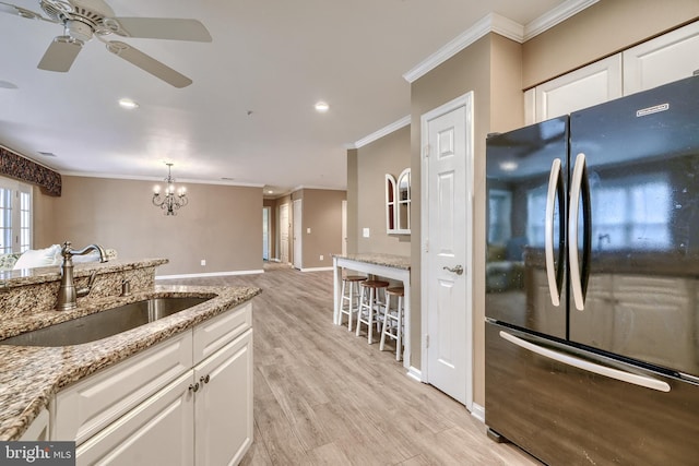 kitchen with sink, black refrigerator, ornamental molding, light hardwood / wood-style floors, and white cabinets