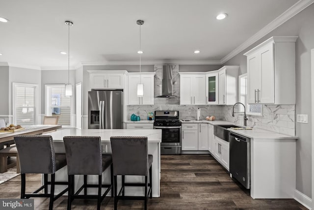 kitchen with a center island, wall chimney range hood, pendant lighting, stainless steel appliances, and white cabinets