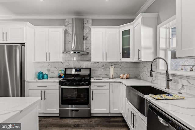 kitchen featuring wall chimney range hood, ornamental molding, stainless steel appliances, and white cabinets