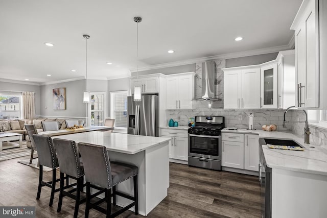 kitchen featuring white cabinetry, appliances with stainless steel finishes, pendant lighting, and wall chimney exhaust hood