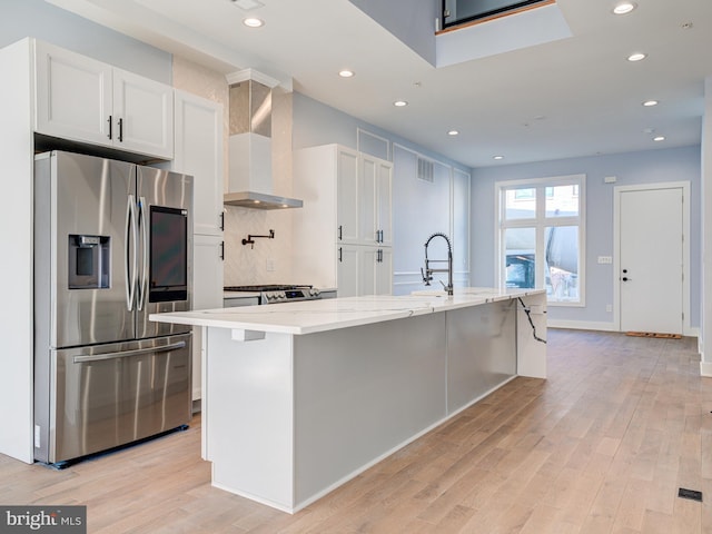 kitchen featuring a center island with sink, wall chimney exhaust hood, white cabinetry, and stainless steel fridge with ice dispenser