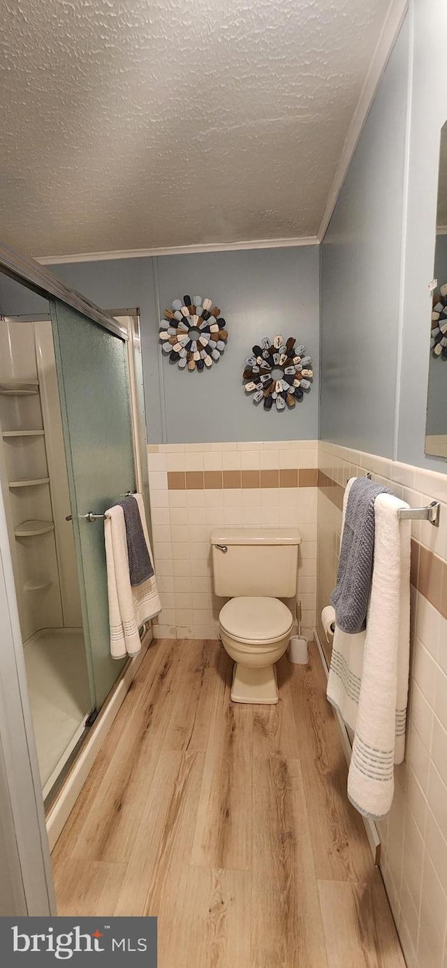 full bathroom featuring tile walls, a wainscoted wall, a textured ceiling, and wood finished floors