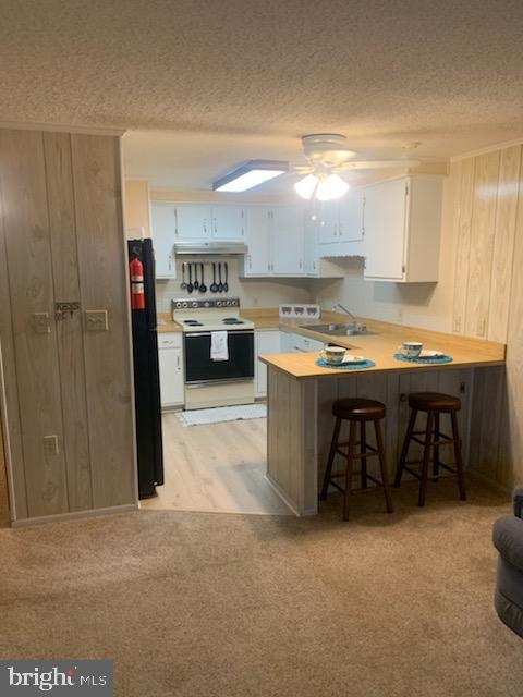 kitchen with white electric stove, light countertops, white cabinetry, a peninsula, and a kitchen breakfast bar