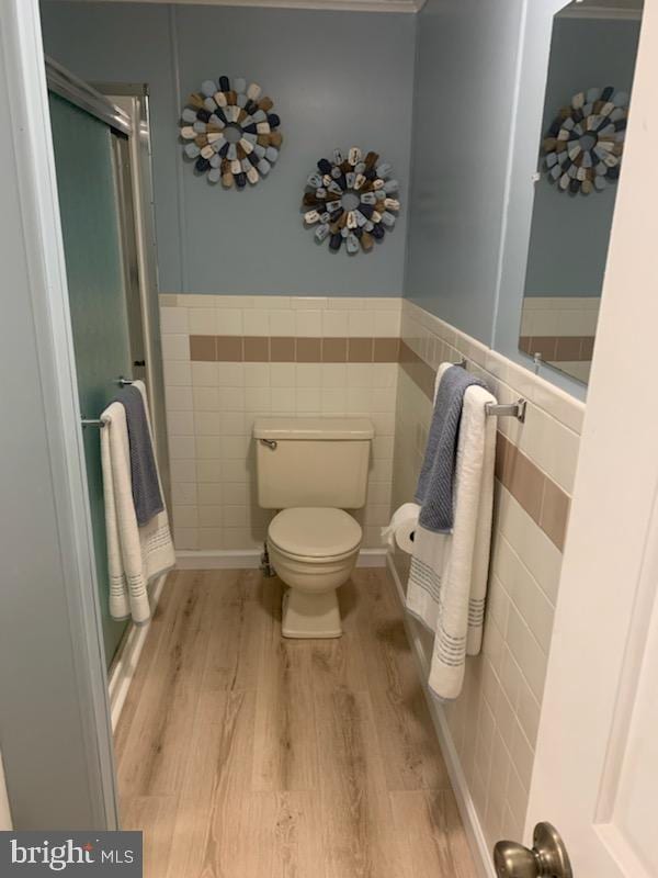 bathroom featuring toilet, wainscoting, wood finished floors, and tile walls