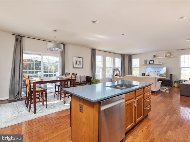 kitchen with dishwasher, sink, a healthy amount of sunlight, a center island with sink, and light wood-type flooring