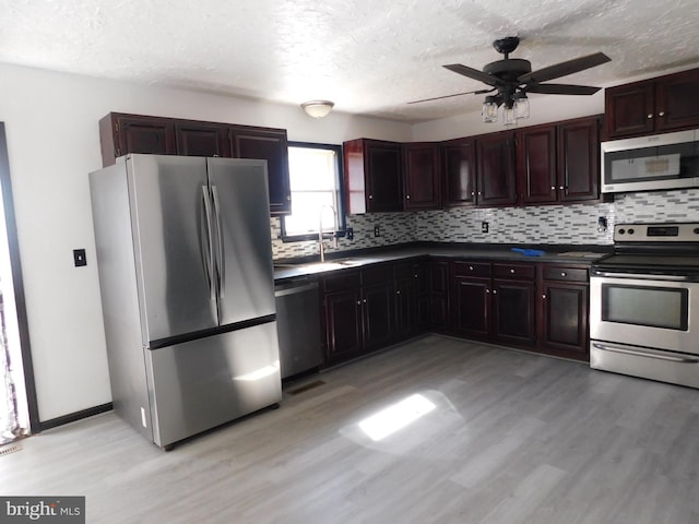 kitchen with light wood finished floors, dark countertops, decorative backsplash, appliances with stainless steel finishes, and a sink