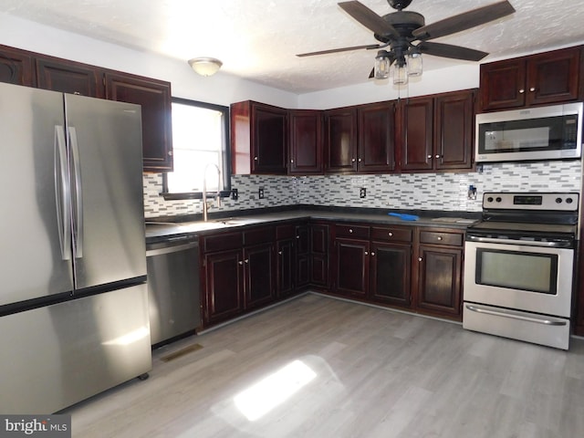 kitchen with light wood-type flooring, appliances with stainless steel finishes, dark countertops, and decorative backsplash