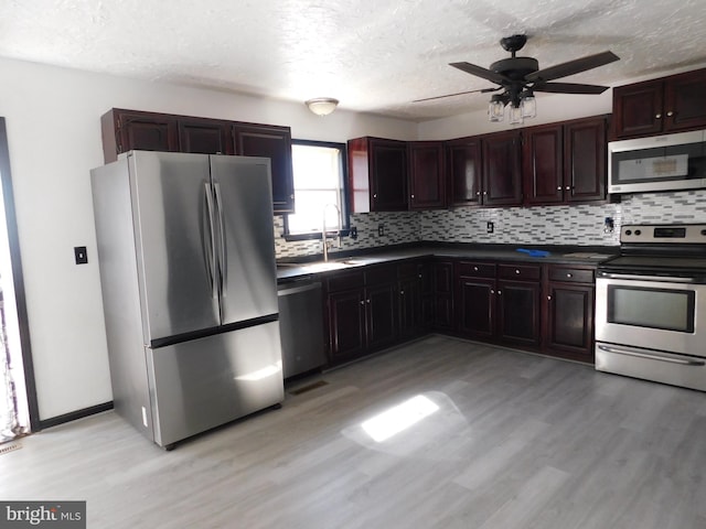 kitchen with a sink, light wood-style floors, appliances with stainless steel finishes, decorative backsplash, and dark countertops