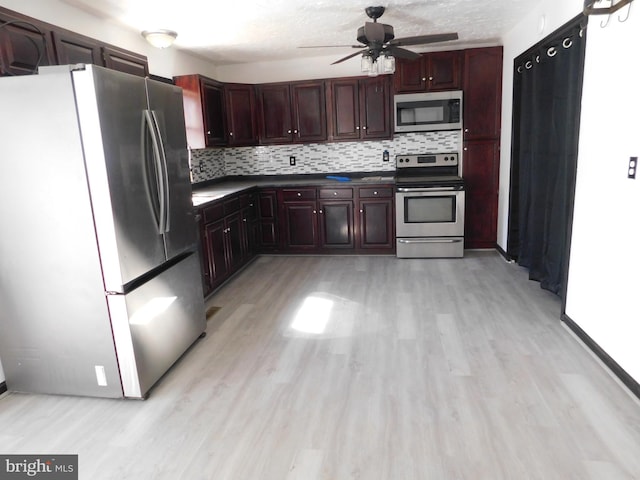 kitchen featuring ceiling fan, appliances with stainless steel finishes, light wood-type flooring, decorative backsplash, and dark countertops