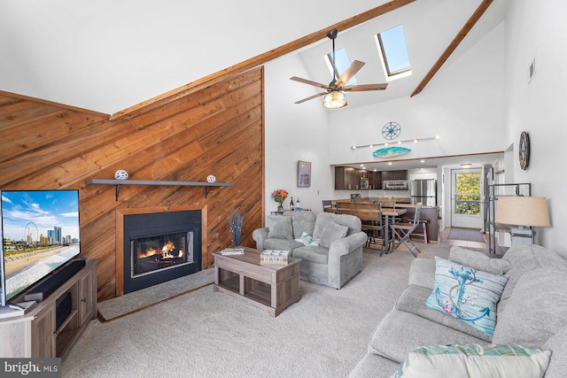 living room with ceiling fan, a skylight, high vaulted ceiling, a fireplace, and light carpet