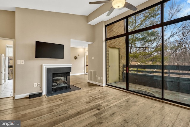 unfurnished living room featuring hardwood / wood-style floors, a towering ceiling, ceiling fan, and a multi sided fireplace