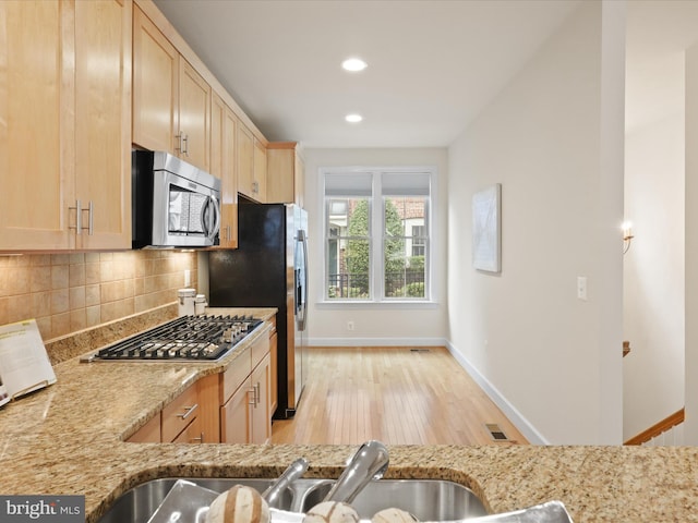 kitchen with decorative backsplash, light brown cabinets, stainless steel appliances, and light stone countertops