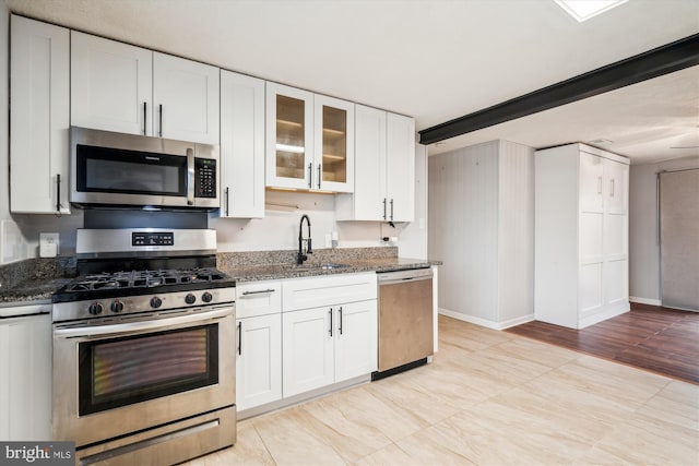 kitchen featuring appliances with stainless steel finishes, sink, white cabinets, and dark stone counters