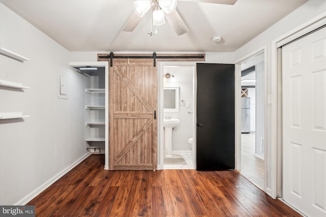 unfurnished bedroom with connected bathroom, a barn door, dark hardwood / wood-style flooring, and a closet