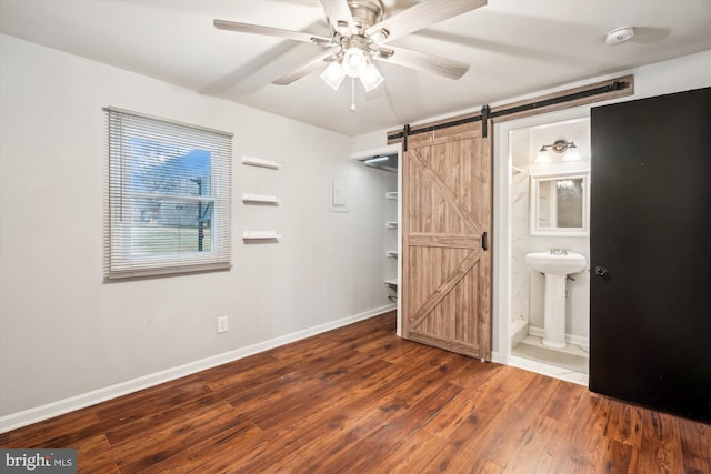 unfurnished bedroom with dark wood-type flooring, sink, ensuite bath, a spacious closet, and a barn door