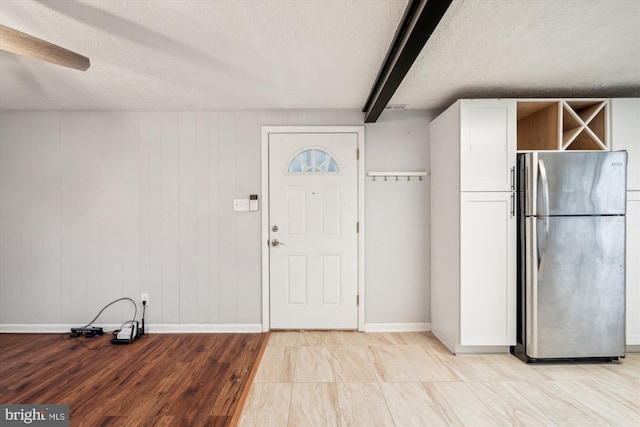 foyer featuring beamed ceiling, light wood-type flooring, and a textured ceiling