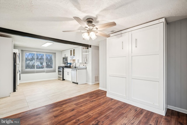 unfurnished living room with ceiling fan, sink, a textured ceiling, and light wood-type flooring