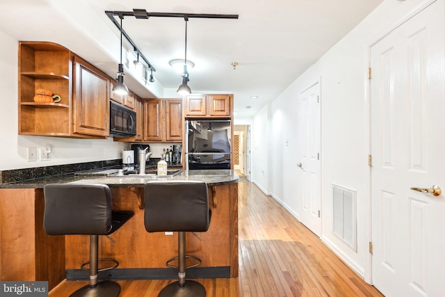 kitchen featuring refrigerator, decorative light fixtures, a kitchen bar, kitchen peninsula, and light hardwood / wood-style flooring