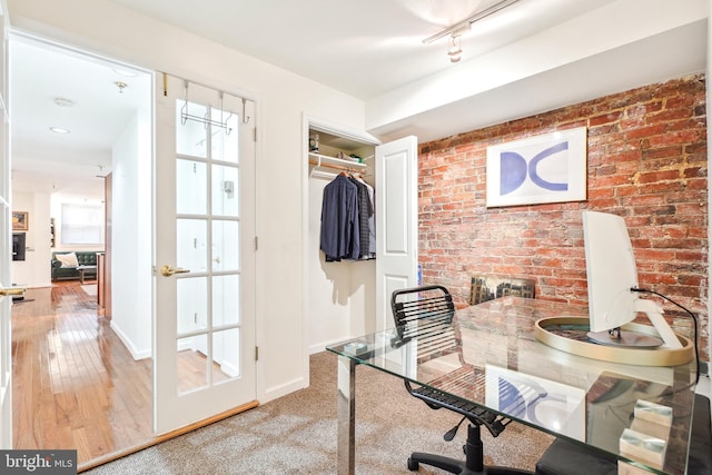 home office with hardwood / wood-style floors, track lighting, and brick wall