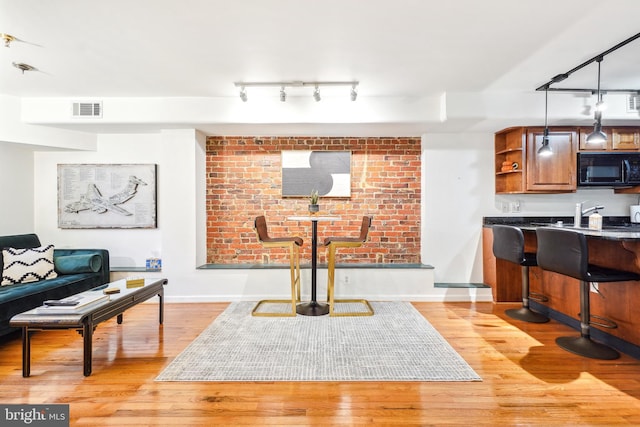 living room with brick wall, sink, light hardwood / wood-style floors, and rail lighting