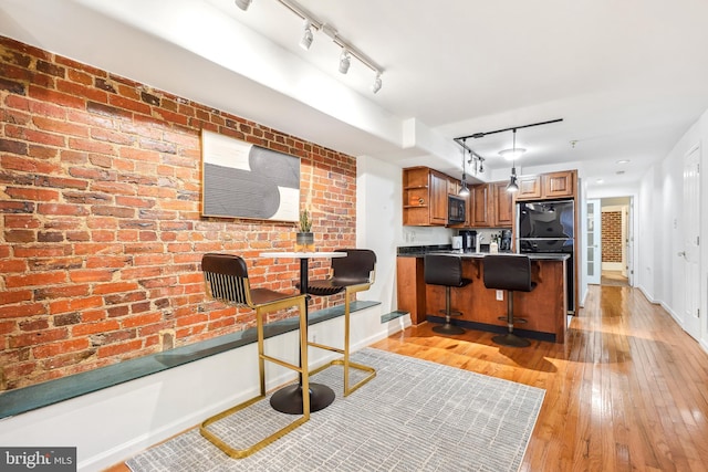 kitchen with brick wall, decorative light fixtures, a kitchen breakfast bar, kitchen peninsula, and light hardwood / wood-style flooring