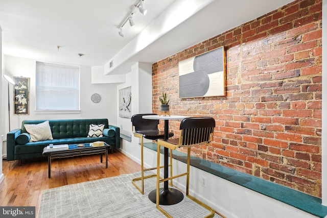 living room with hardwood / wood-style floors, rail lighting, and brick wall